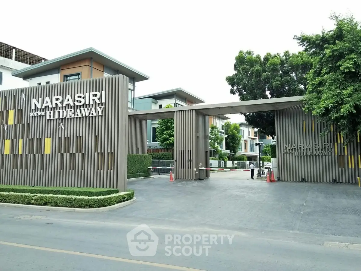 Modern gated entrance of Narasiri Hideaway with lush greenery and contemporary architecture.