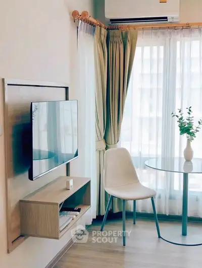 Modern living room with wall-mounted TV, elegant chair, and glass table near window.
