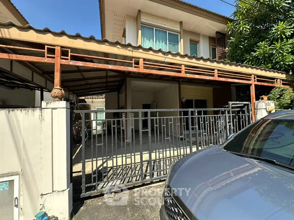 Charming two-story house with gated entrance and carport in a sunny neighborhood.