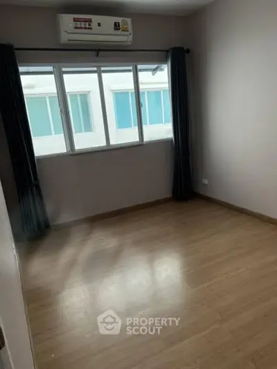 Spacious empty room with wooden flooring and large window, ideal for customization.