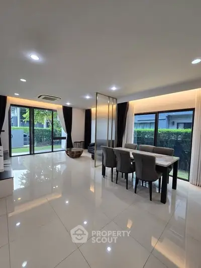 Spacious modern living room with dining area and large windows overlooking greenery.