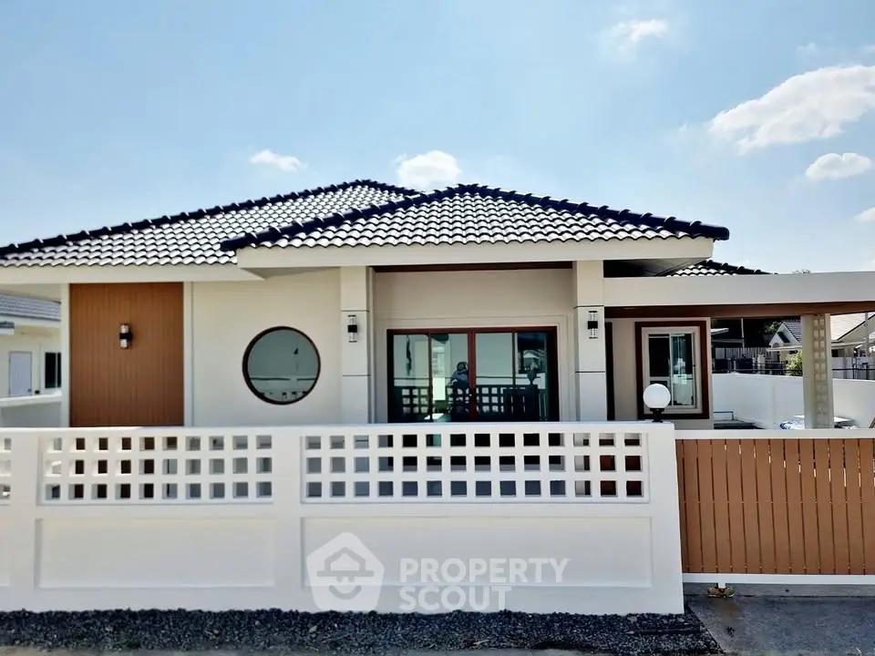 Modern single-story house with stylish roof and fenced yard under clear blue sky.