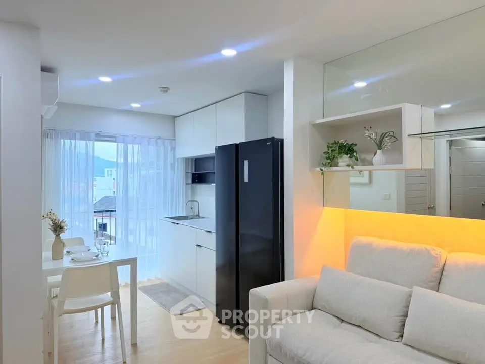 Modern open-layout living room with sleek kitchen and cozy dining area, featuring natural light and stylish decor.