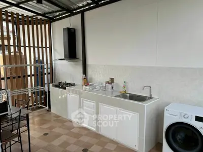 Modern outdoor kitchen with gas stove and washing machine in a sleek open layout.