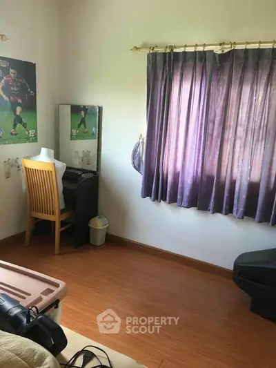 Cozy bedroom with wooden flooring and purple curtains, featuring a small vanity and chair.