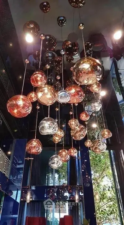 Stunning modern chandelier in luxurious living room with floor-to-ceiling windows and lush greenery view.