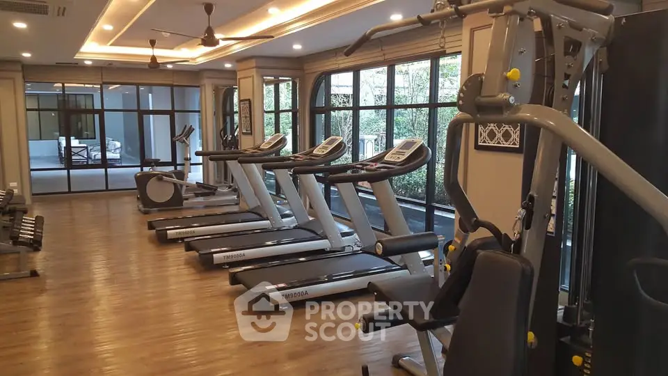 Spacious gym with modern equipment and large windows in luxury residential building.