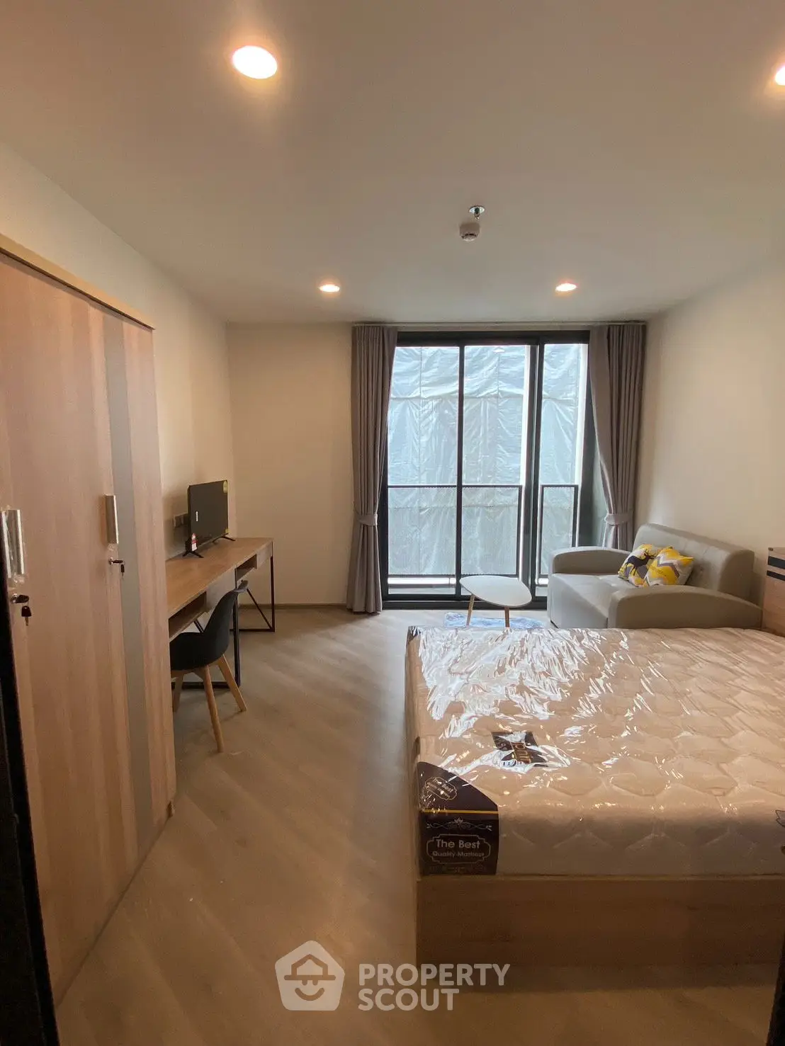 Modern bedroom with large window, cozy sofa, and workspace in stylish apartment.