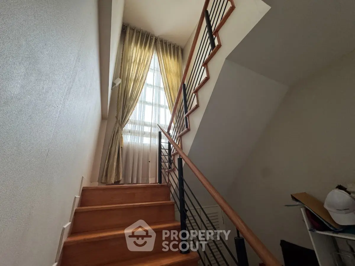 Elegant staircase with wooden steps and stylish railing leading to a sunlit window with curtains.