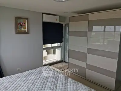 Modern bedroom with large bed, expansive built-in wardrobe, and access to a sunlit balcony, perfect for urban living.