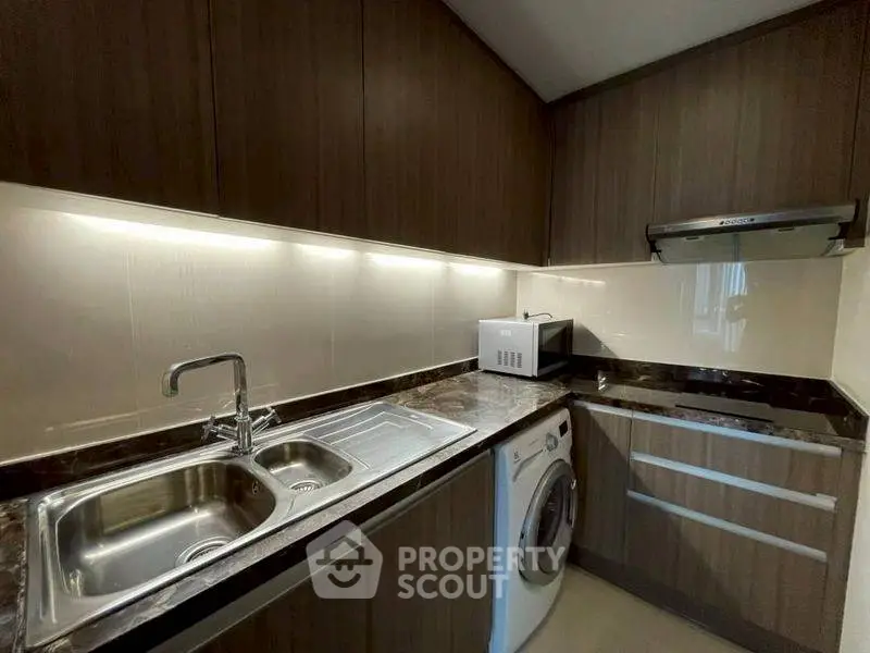 Modern kitchen with sleek cabinets, washing machine, and microwave in compact layout.