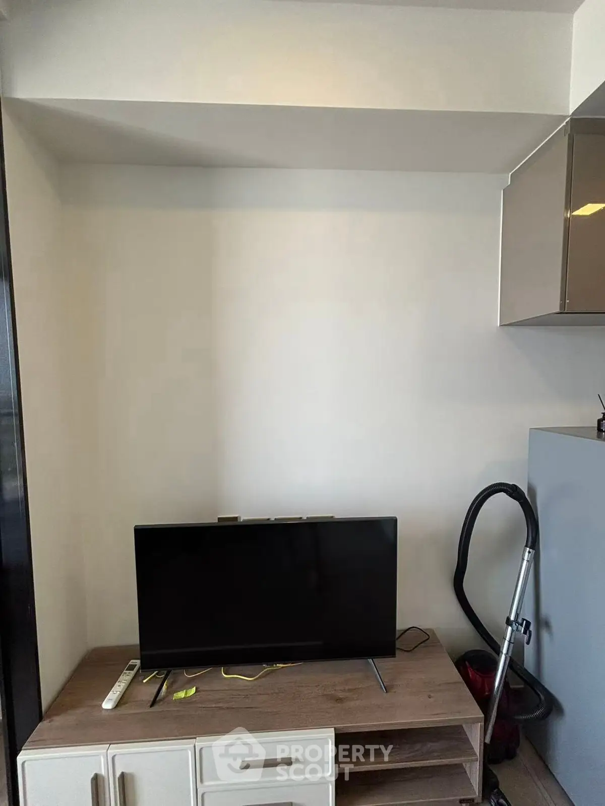 Modern living room with sleek TV setup and vacuum cleaner, perfect for minimalist lifestyle.