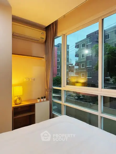 Cozy bedroom with large window offering urban view and natural light.