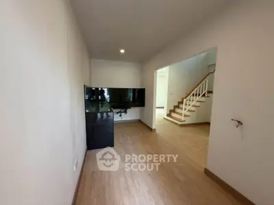 Spacious living room with modern TV setup and wooden flooring, leading to a staircase.