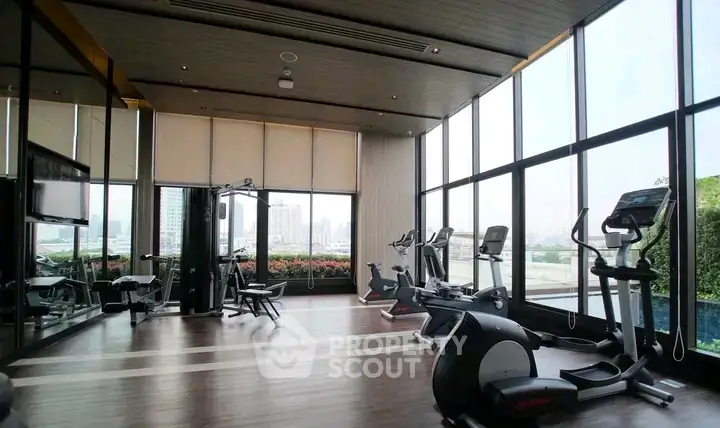 Spacious gym with modern equipment and city view in luxury apartment building.