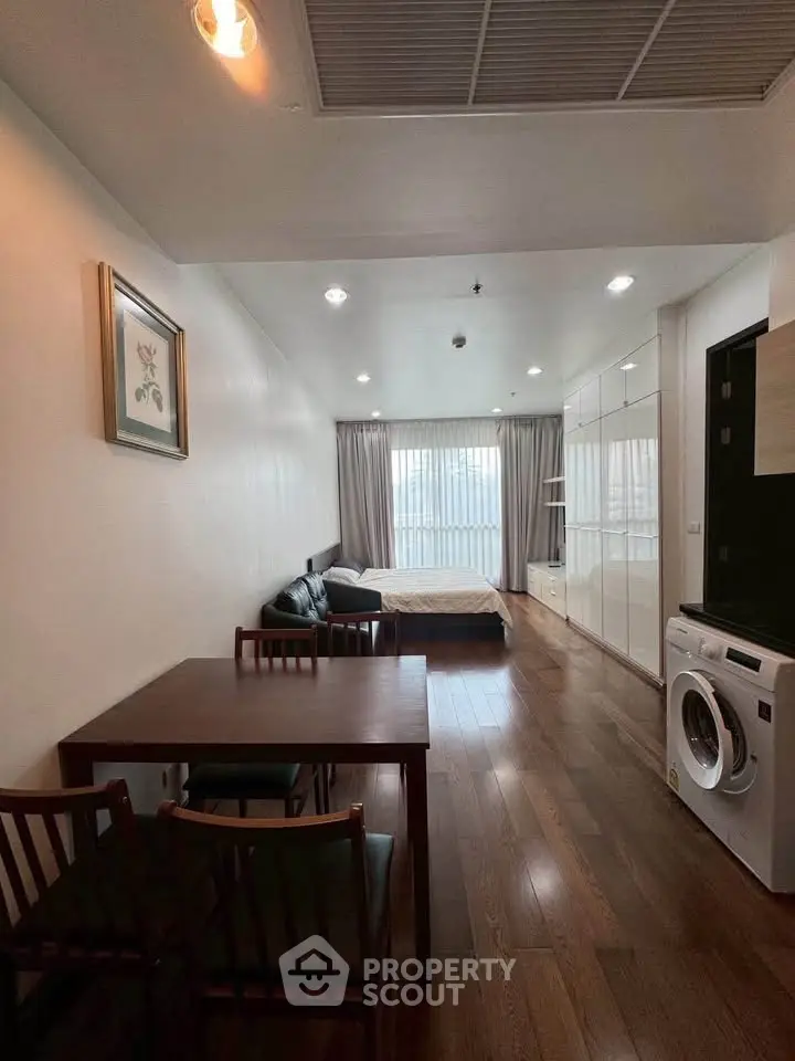 Modern studio apartment with wooden flooring, dining area, and washing machine, offering a cozy living space.