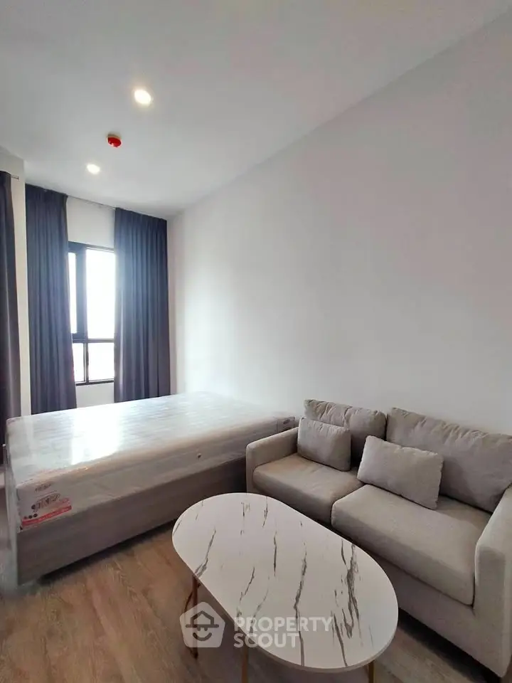 Modern bedroom with cozy sofa and stylish coffee table, natural light from large window.