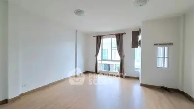 Spacious empty room with large window and wooden flooring in modern apartment.
