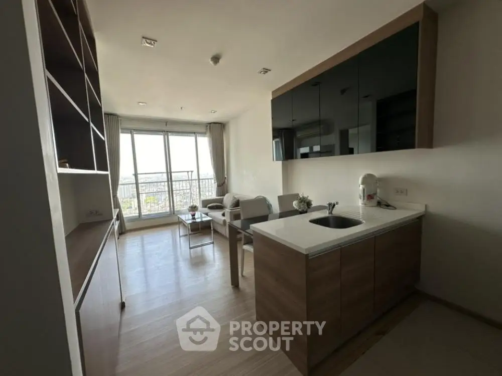 Modern living room with open kitchen and balcony view, featuring sleek cabinetry and stylish decor.