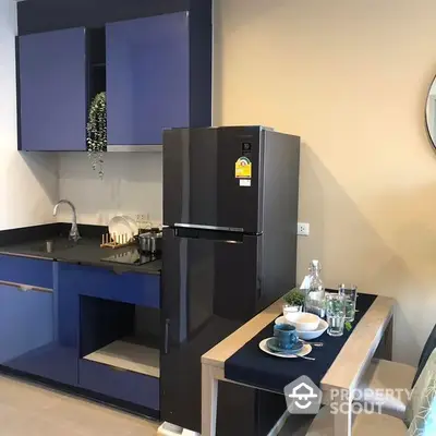 Modern kitchen with sleek blue cabinetry, stainless steel gas stove, and a large fridge, complemented by a cozy dining area.