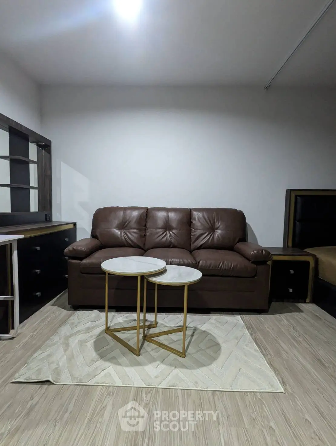 Modern living room with brown leather sofa and stylish nested tables on a chic rug.
