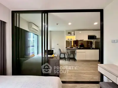 Modern open-plan apartment with sleek kitchen and cozy living area, featuring large windows and stylish decor.