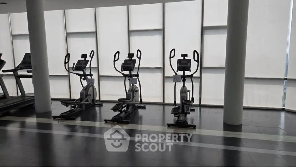 Modern gym with exercise equipment and large windows in a luxury apartment building.