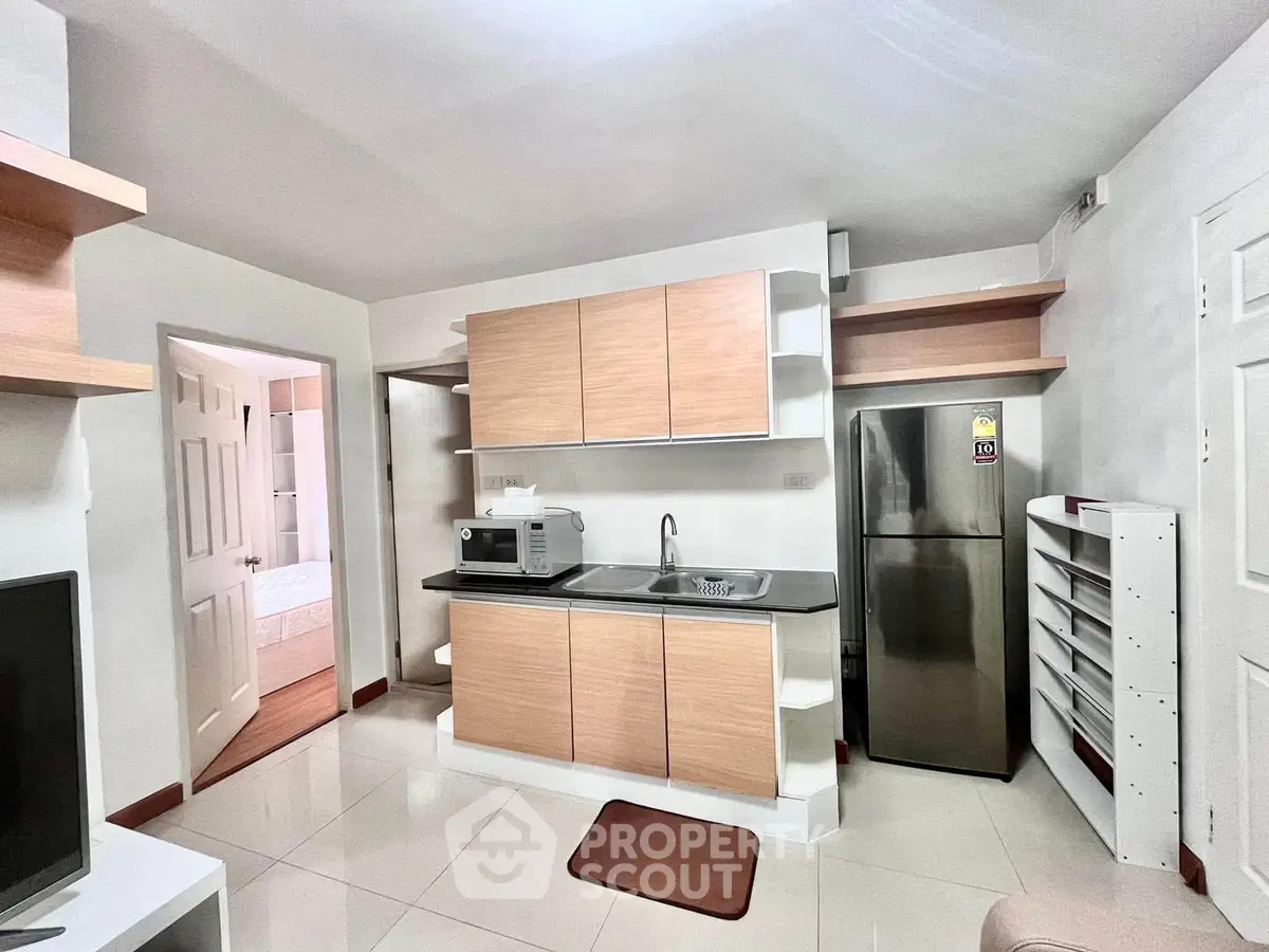 Modern compact kitchen with stainless steel fridge and microwave in cozy apartment.