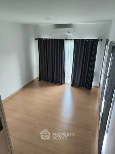 Spacious empty room with wooden flooring and large windows, perfect for customization.
