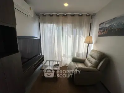 Cozy living room with modern decor, featuring a comfortable armchair, large TV, and natural light through sheer curtains.