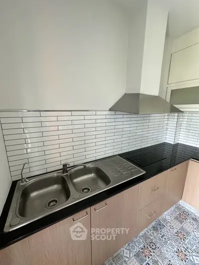 Modern kitchen with sleek black countertop and stainless steel sink, featuring stylish tiled backsplash.