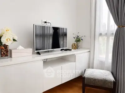 Elegant living room corner with modern TV setup and natural light from large window.
