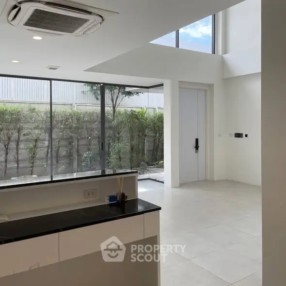 Modern open-plan living area with large windows and garden view, featuring sleek design and abundant natural light.