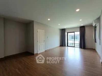 Spacious empty living room with wooden flooring and large windows for natural light.