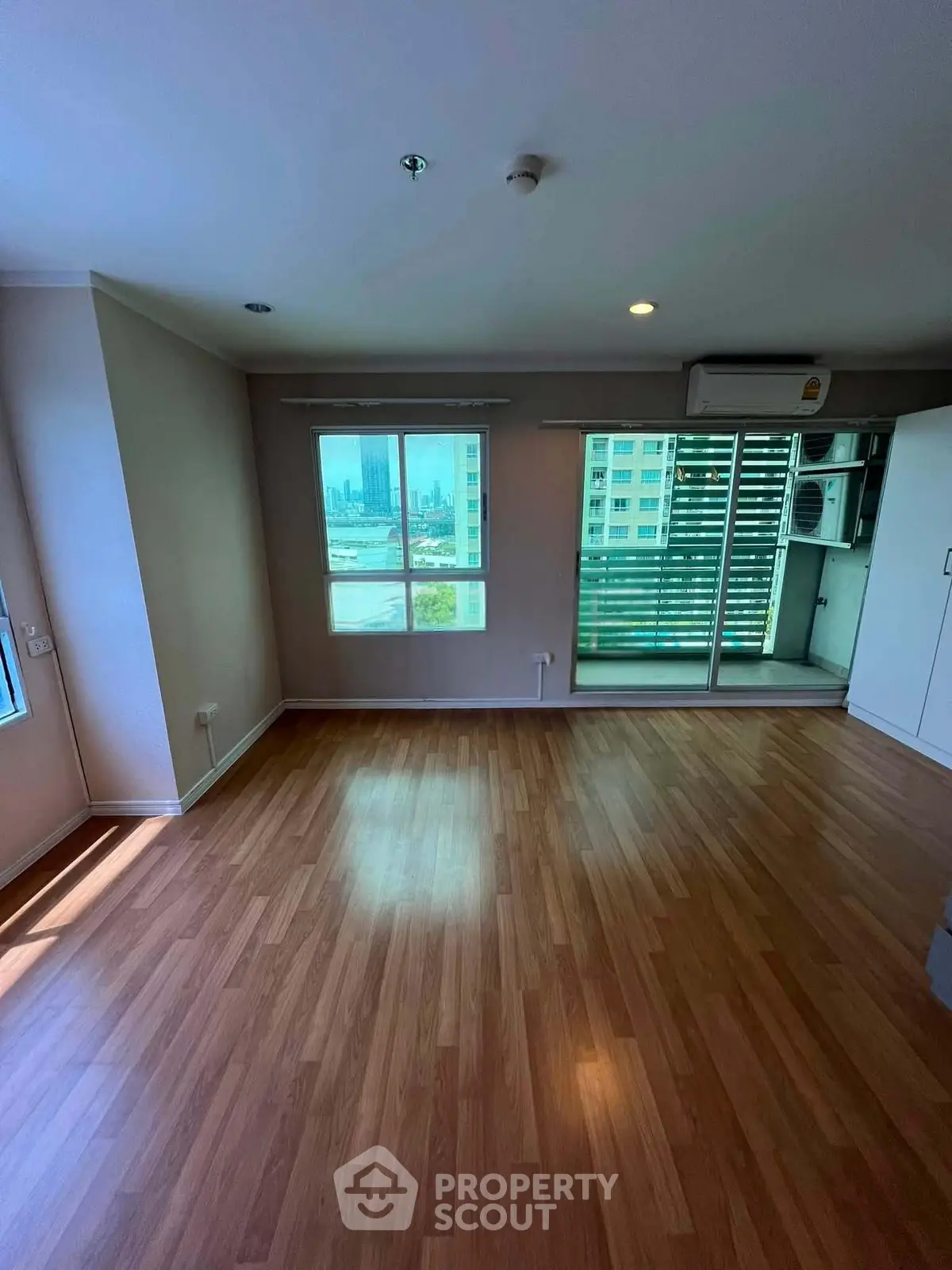 Spacious living room with wooden flooring and large windows offering city views.