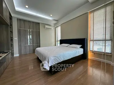 Spacious modern bedroom with wooden flooring and large windows for natural light.
