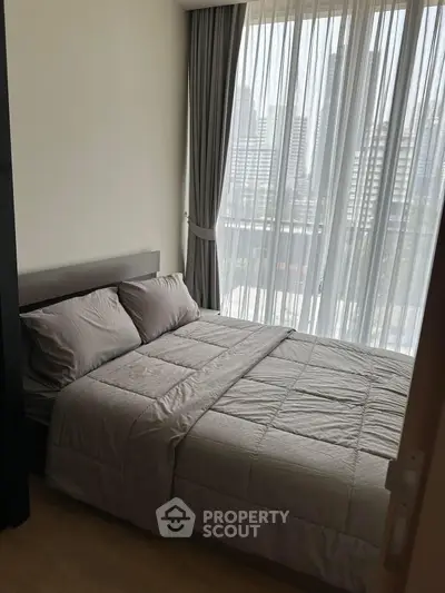 Cozy bedroom with city view through sheer curtains, perfect for urban living.