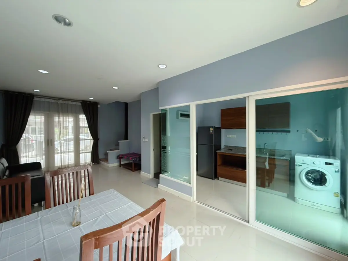 Modern open-plan living room with kitchen and washing machine, featuring sleek design and ample natural light.