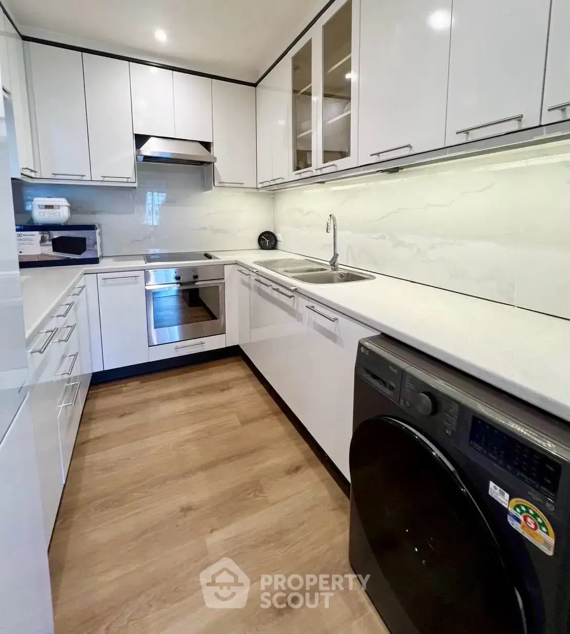 Modern kitchen with sleek white cabinets, built-in appliances, and wooden flooring.