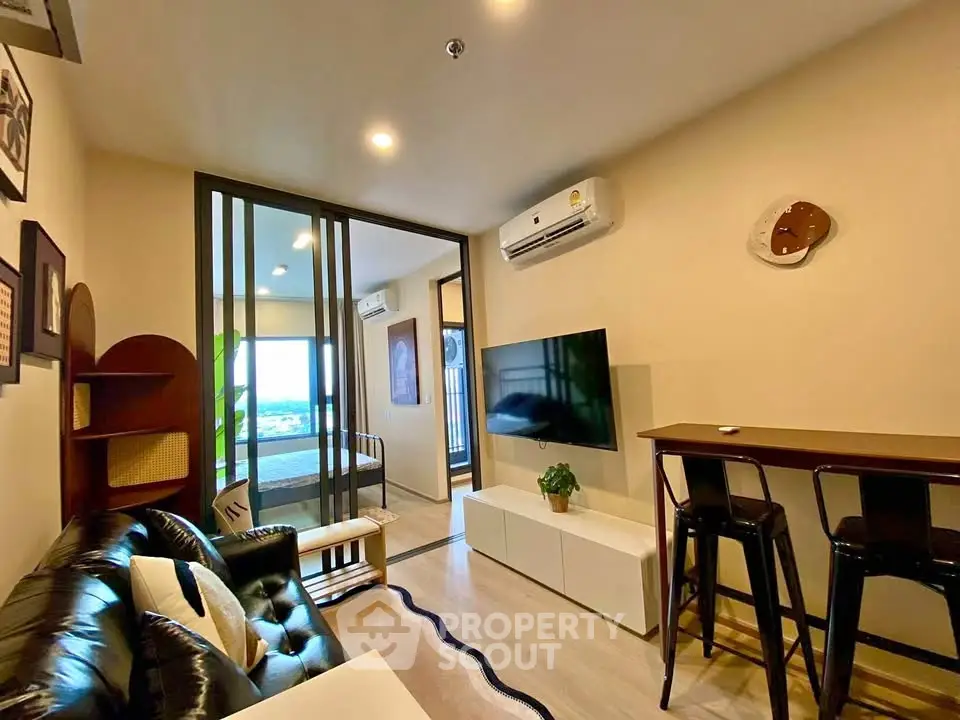 Modern living room with stylish decor and open view to bedroom, featuring sleek furniture and wall-mounted TV.