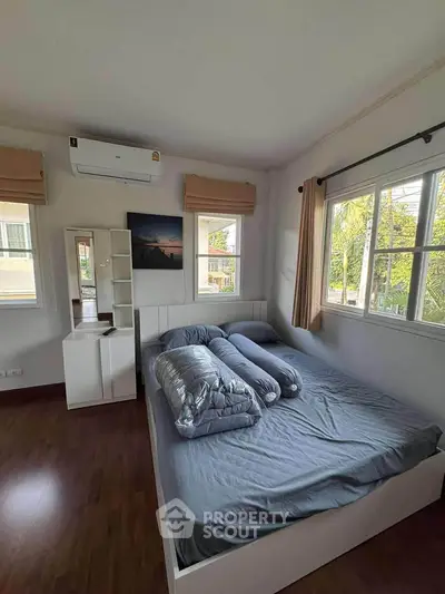 Cozy bedroom with large windows and natural light, featuring a stylish bed and air conditioning.
