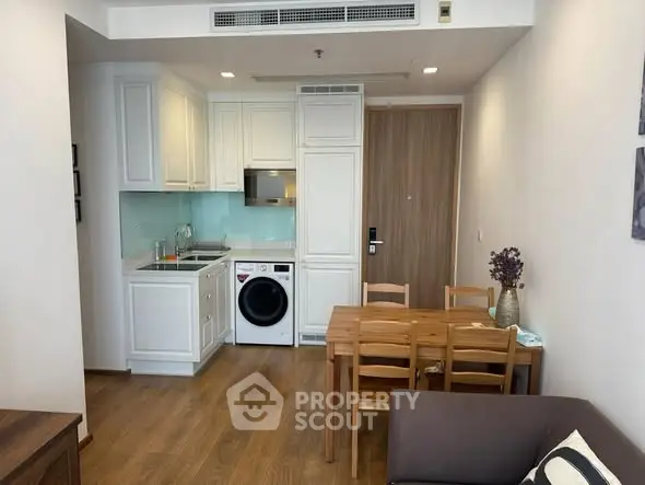 Modern compact kitchen with integrated appliances and dining area in cozy apartment.