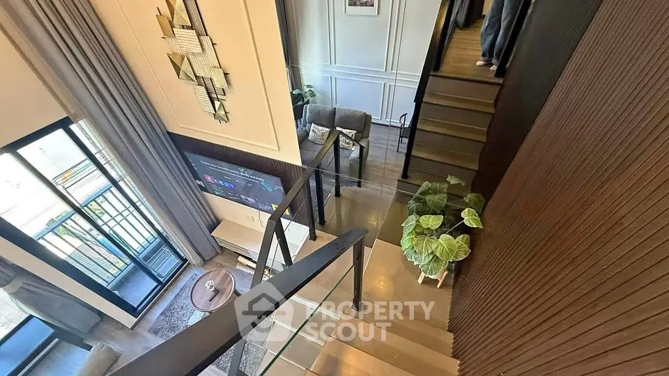 Modern duplex interior with stylish staircase and cozy living area, featuring large windows and elegant decor.