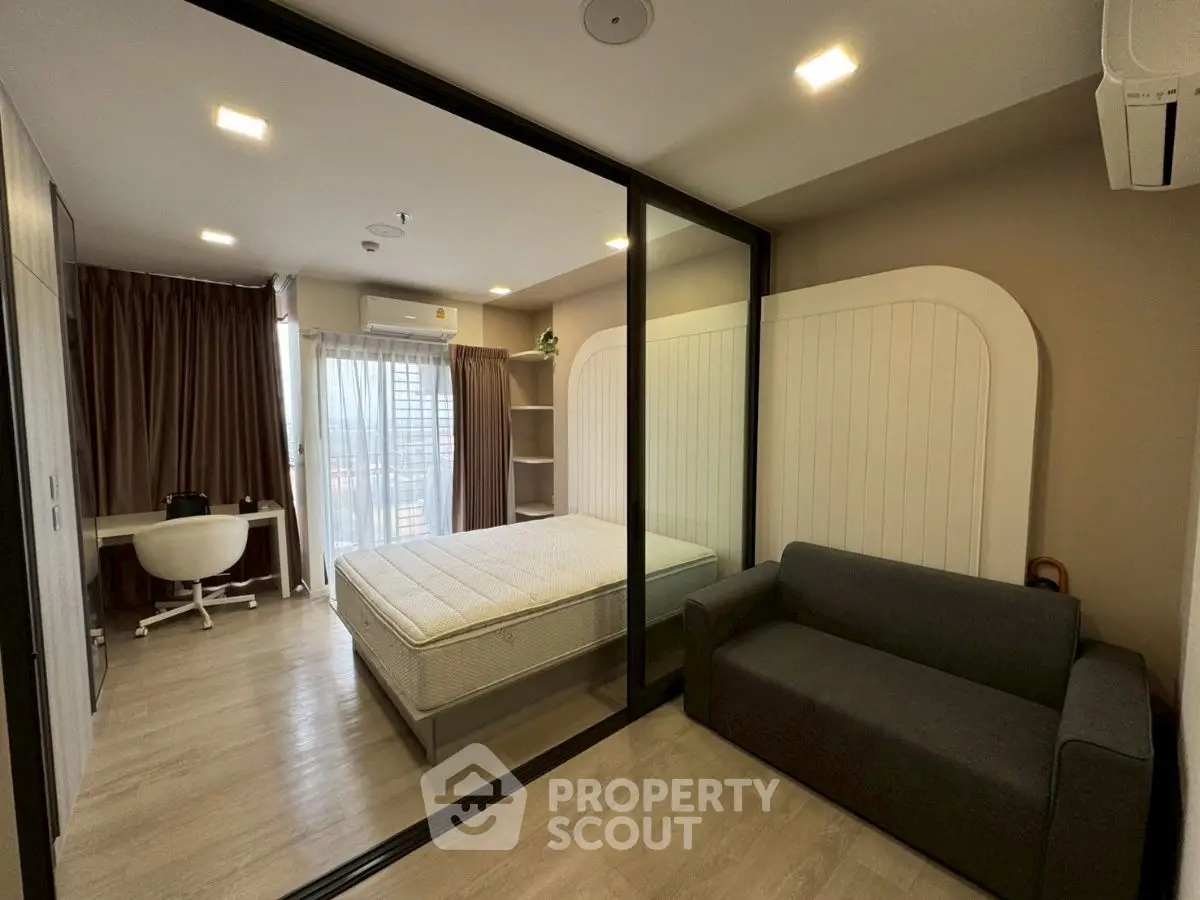 Modern bedroom with glass partition, cozy sofa, and stylish workspace.
