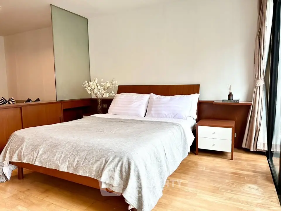 Spacious bedroom with wooden flooring and modern furnishings in a bright apartment.