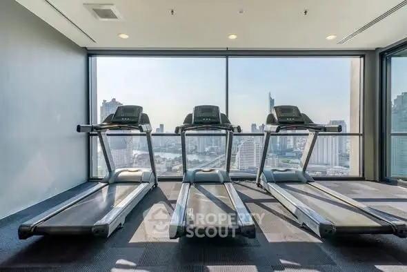 Modern gym with city view featuring three treadmills and large windows.