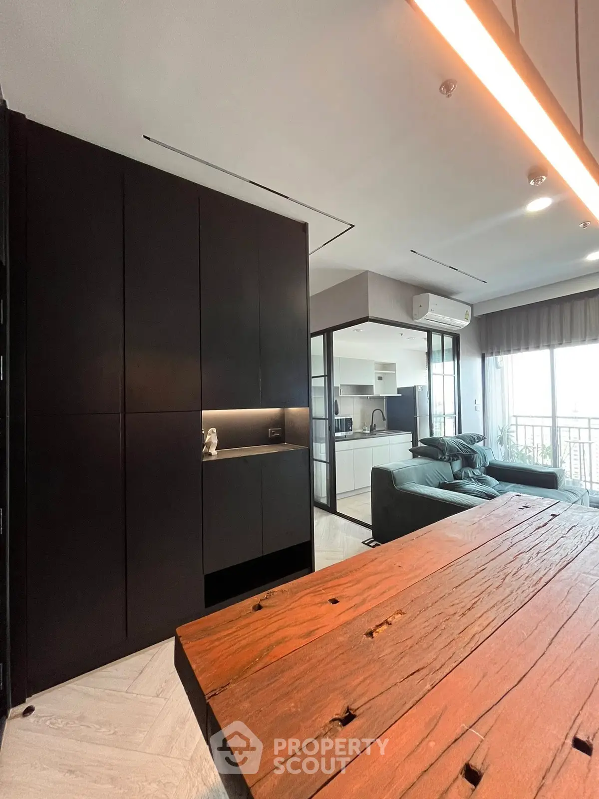 Modern open-plan living room with sleek kitchen and rustic wooden table, featuring stylish black cabinetry.