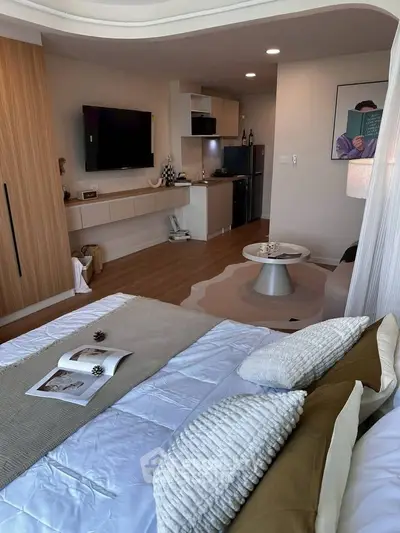 Modern studio apartment with cozy bedroom and open kitchen layout, featuring stylish decor and a wall-mounted TV.