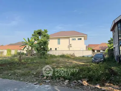 Spacious plot with potential for development, featuring a modern house and lush greenery in a serene neighborhood.