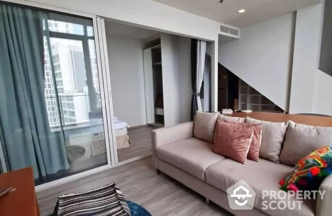 Spacious living room with modern sofa, large windows leading to a sunny balcony, and sleek hardwood flooring, perfect for urban living.